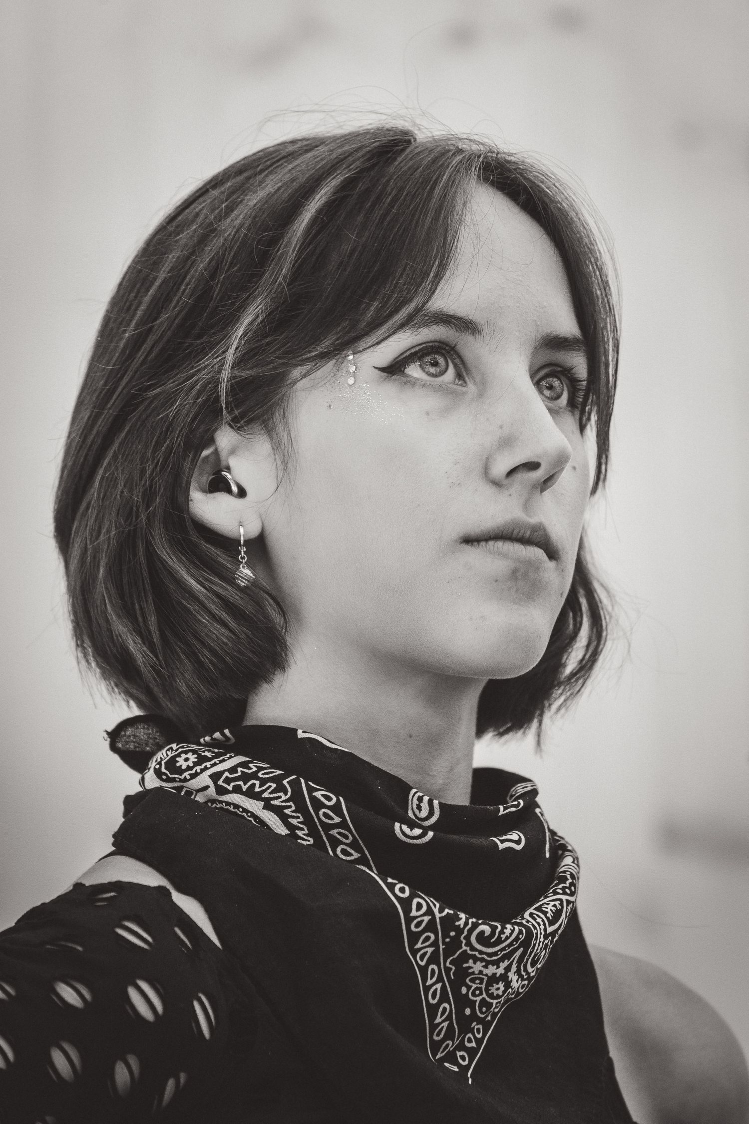 Black and white portrait of young woman with short hair and bandana scarf looking up.