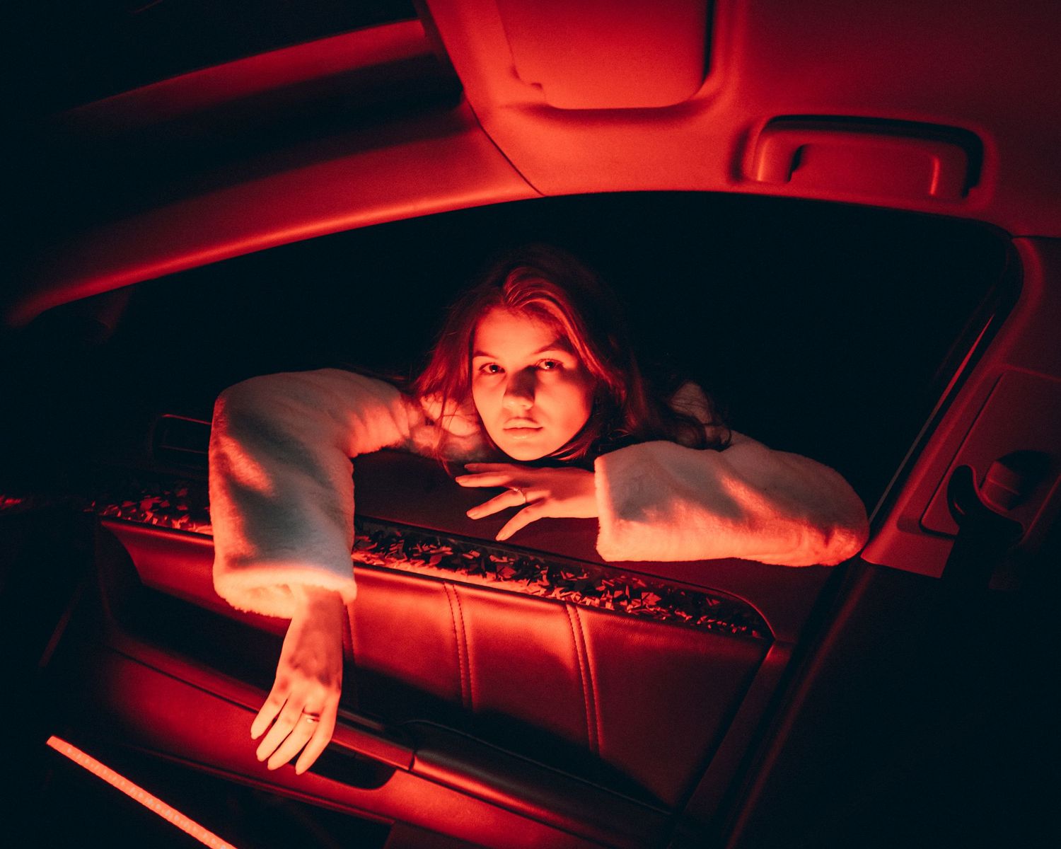 Woman leaning out of a car window bathed in moody red neon light at night.