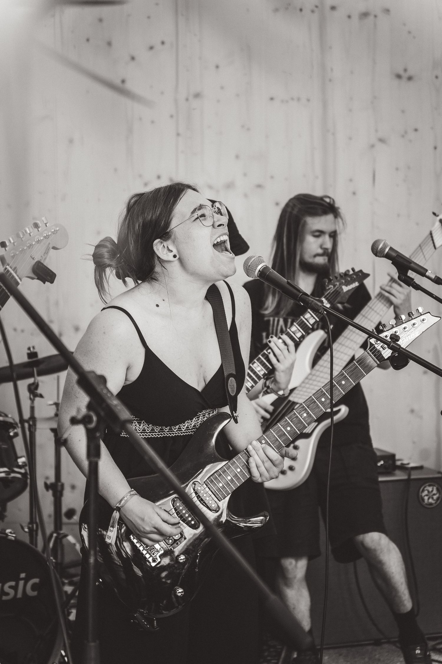 Black and white photo of female vocalist singing and playing guitar with band member behind her.
