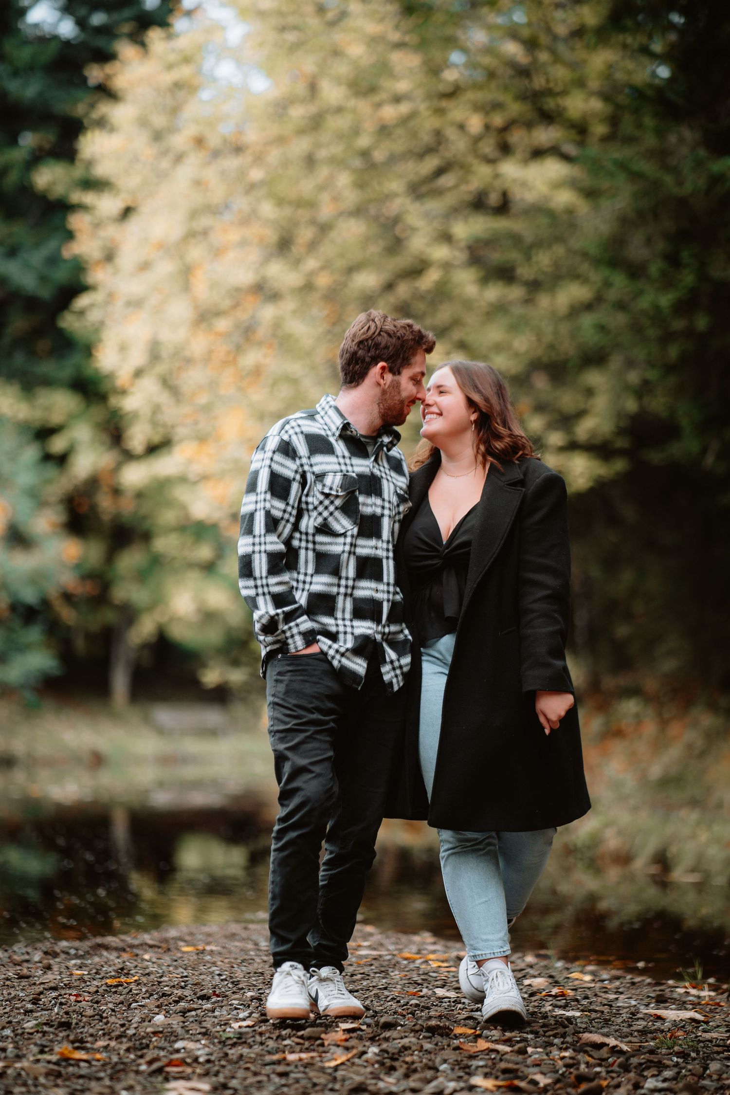 Couple sharing a romantic moment on a tree-lined autumn path in casual outdoor attire.