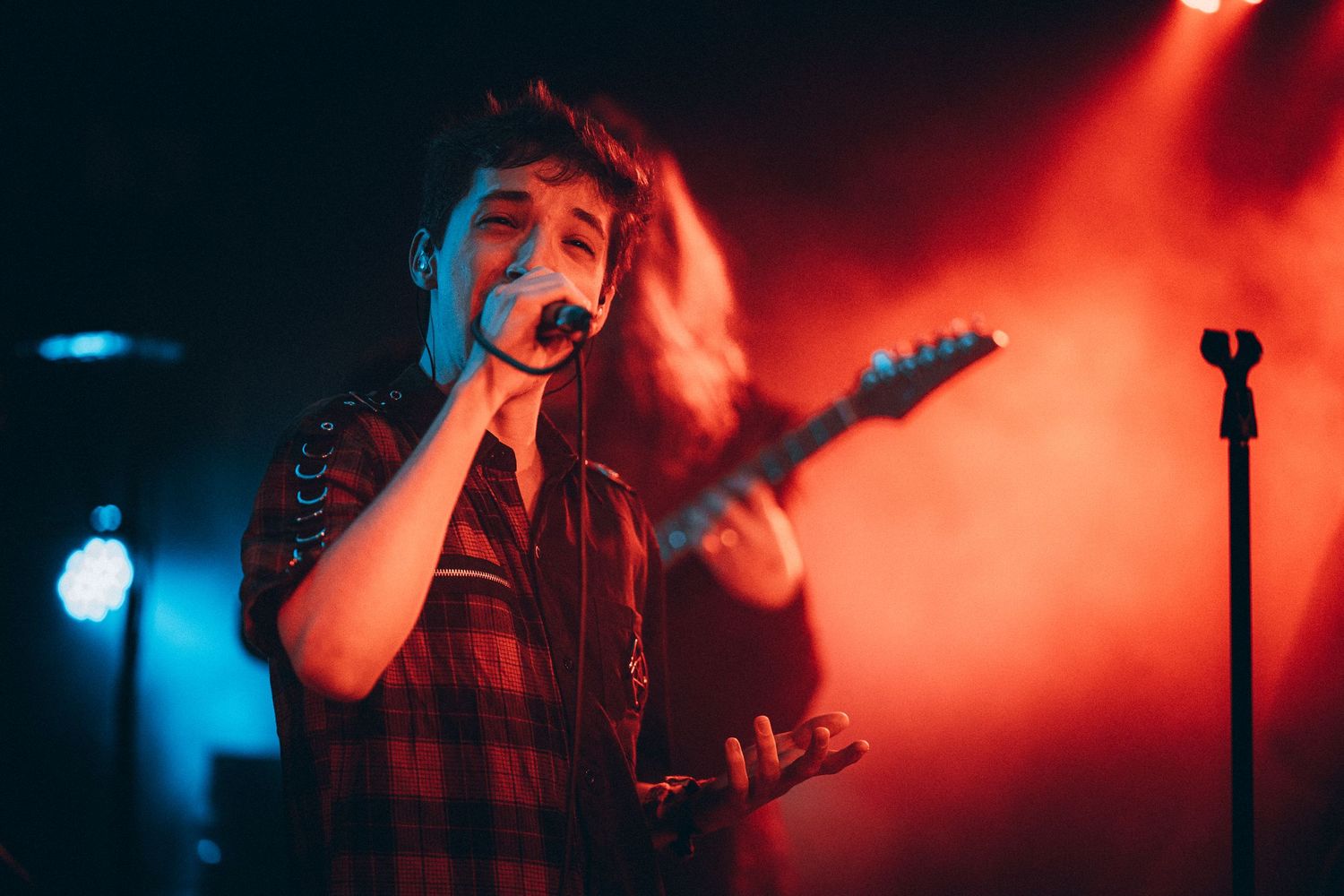 Female vocalist singing into microphone with guitarist performing under colorful stage lights.