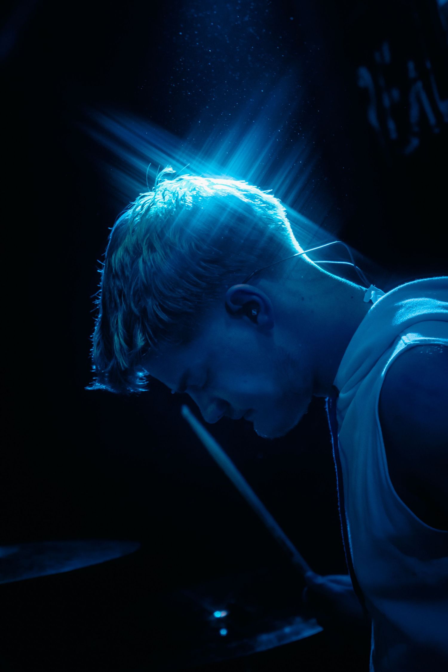 Drummer illuminated by blue spotlight while playing at a dark concert venue.