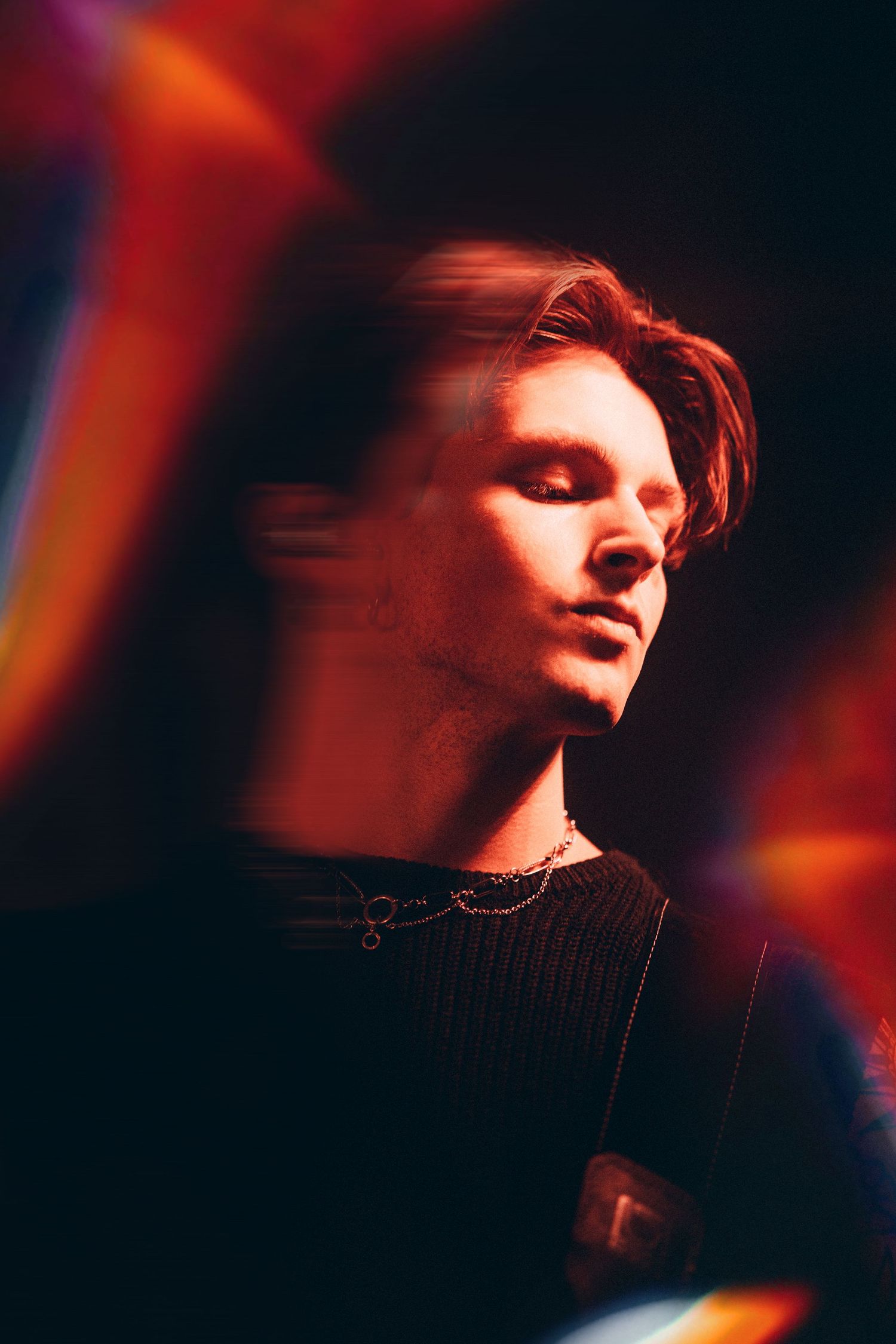 Young male musician with eyes closed bathed in warm red concert lighting.