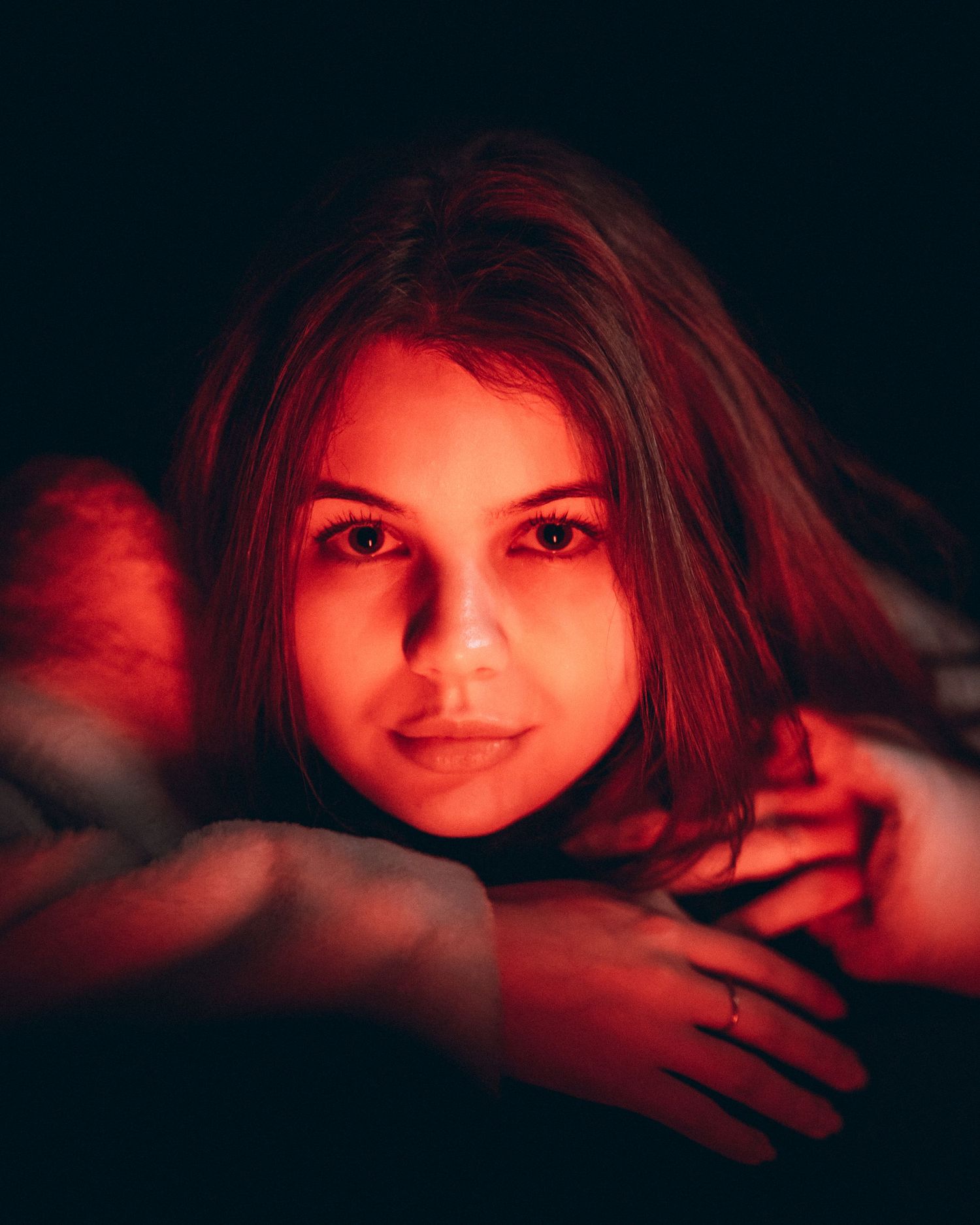 Young woman with brown hair illuminated by dramatic red lighting in a dark studio portrait.