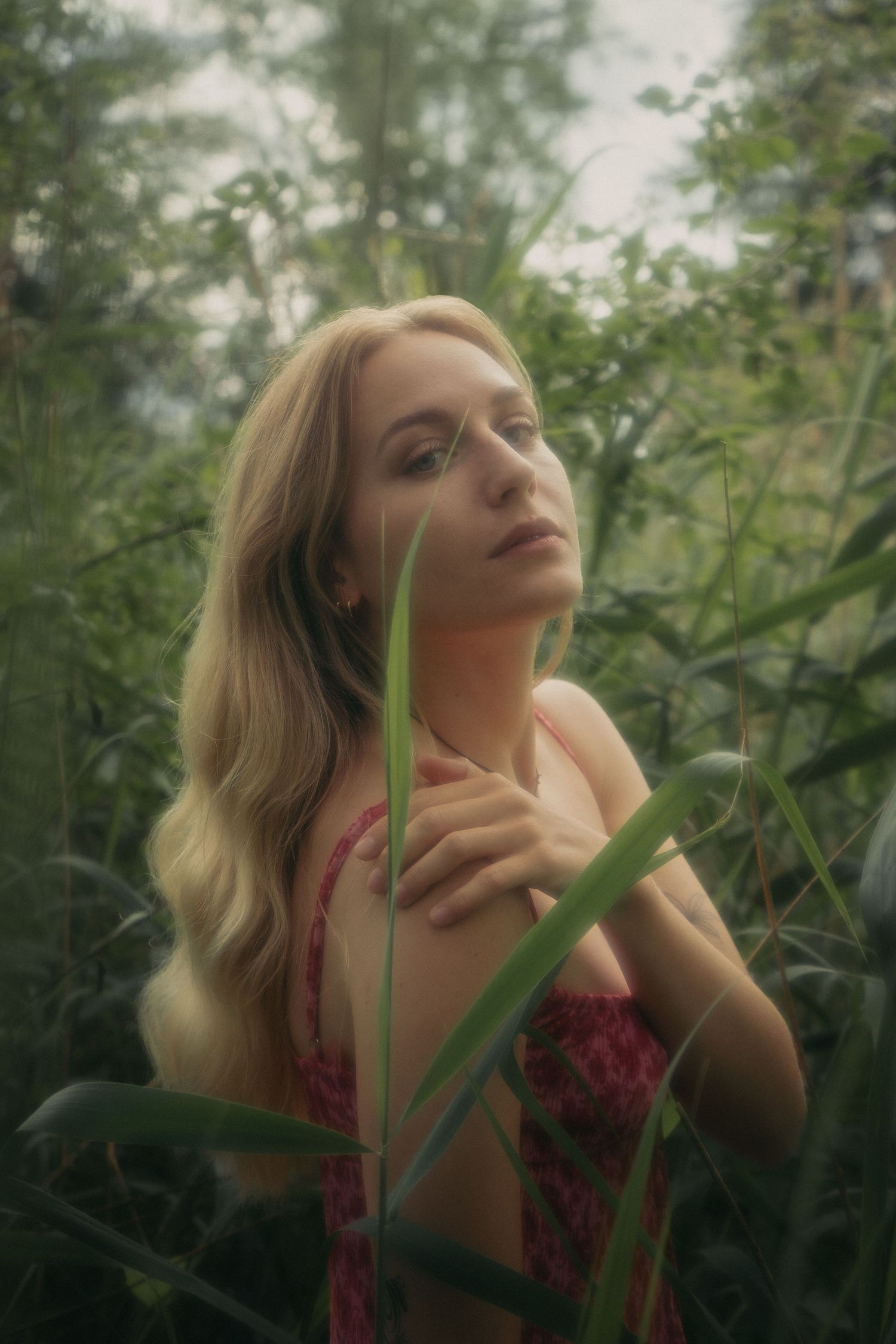 Blonde woman in floral dress surrounded by lush green foliage in a dreamy forest portrait.