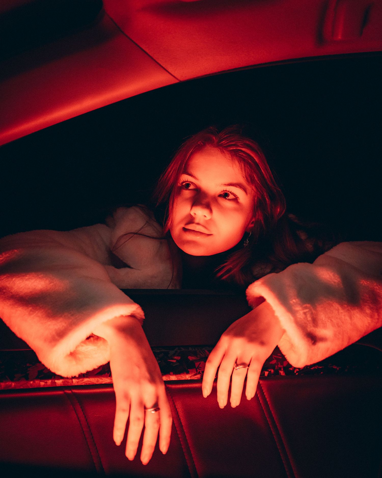 Woman peering through a car window with hands resting on the ledge in red light.