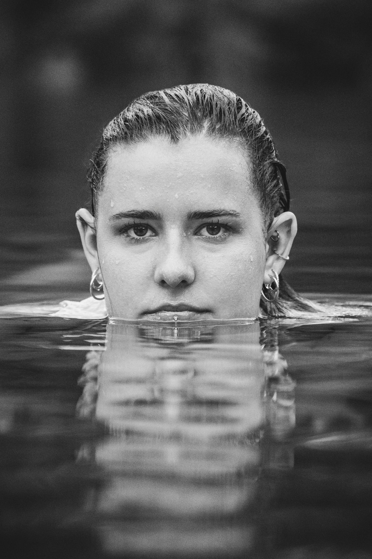 Black and white portrait of a woman submerged in water with only her face visible above surface.