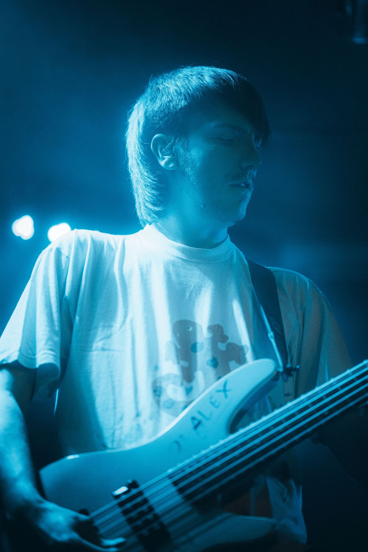 Bass guitarist in white t-shirt performing under cool blue stage lighting.
