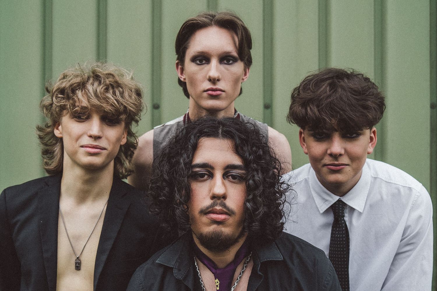 Four young musicians posing together in front of green wall for band promotional photo.