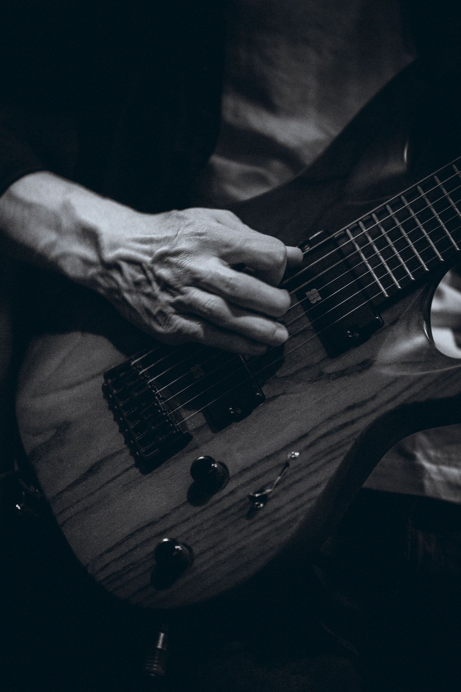 Black and white close-up of hands playing a wooden electric guitar on stage.