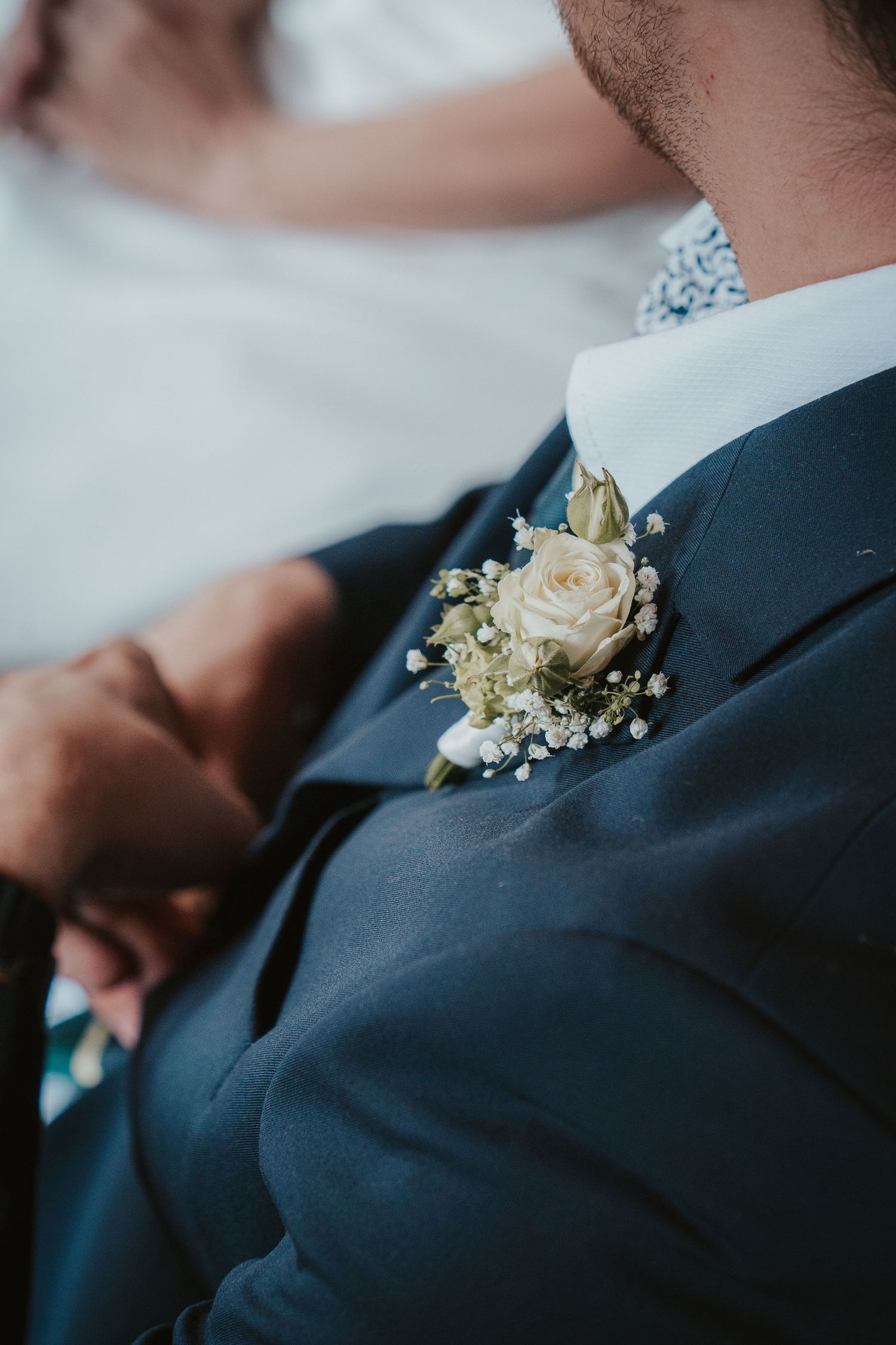 Close-up of groom in navy suit with elegant white rose and baby's breath boutonniere on lapel.