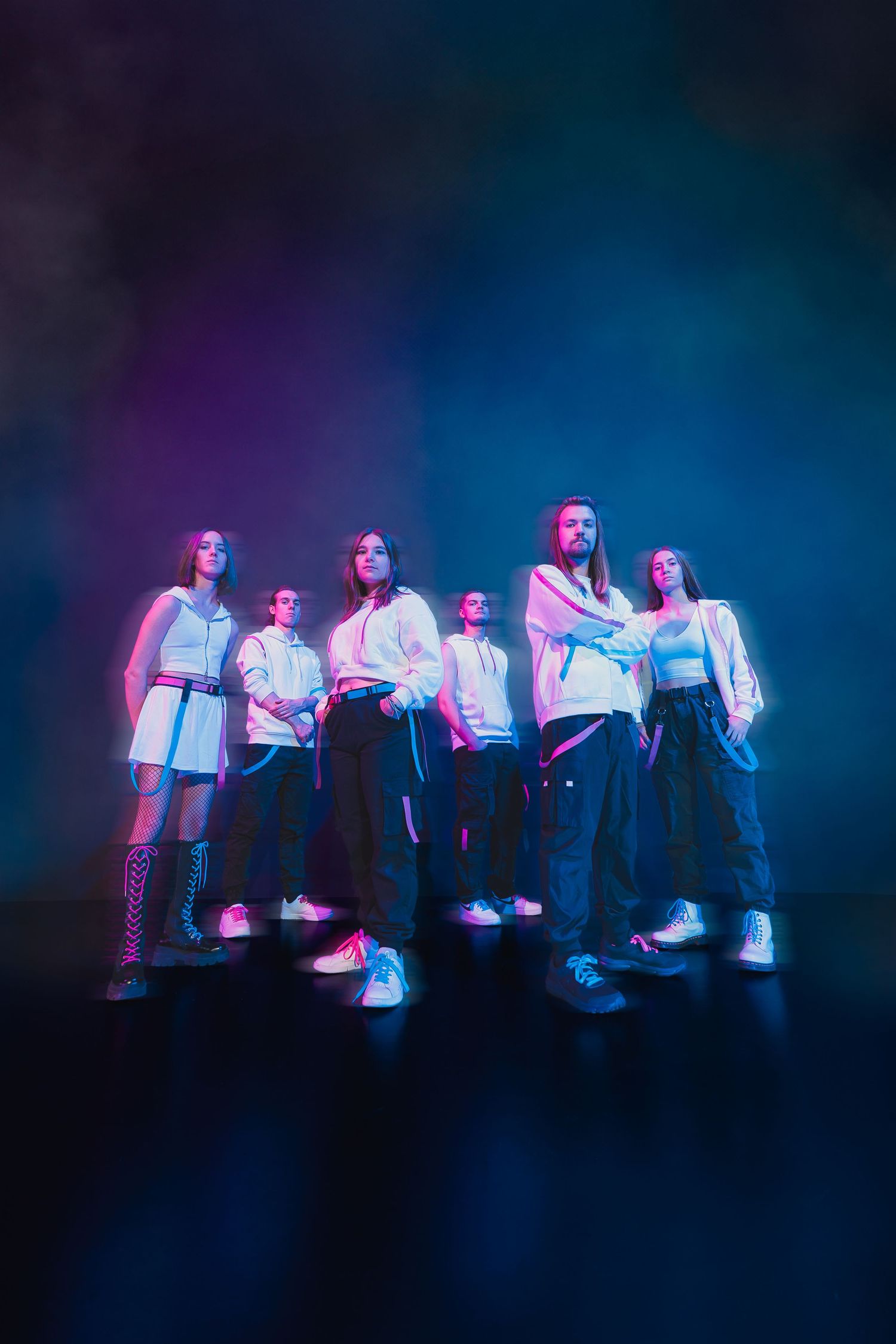 Group of six performers posing under colorful blue and purple smoke-filled stage lights.