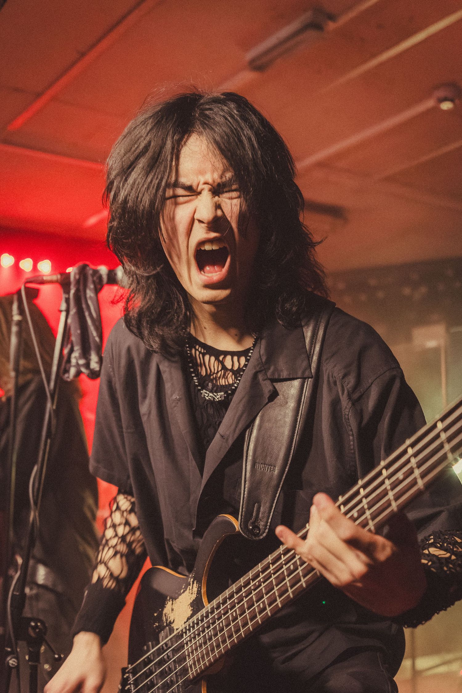 Rock guitarist with long black hair screaming passionately while playing bass guitar on stage.