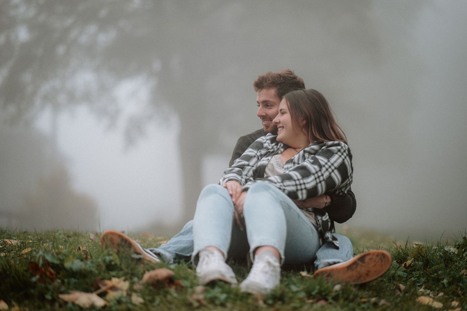 Romantic couple sitting together on grass in misty autumn park embracing affectionately.