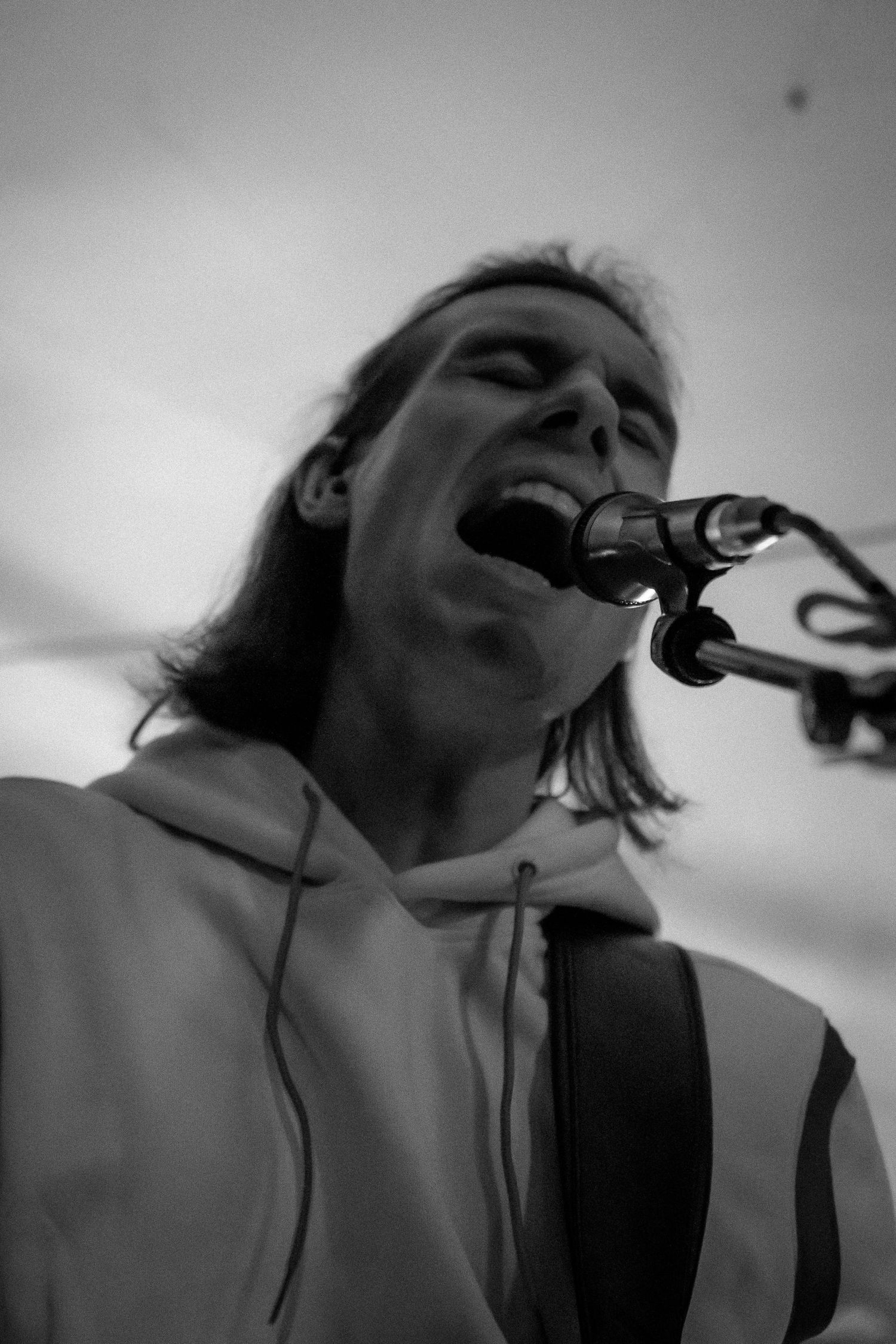 Black and white close-up of a long-haired musician singing passionately into a microphone while playing guitar.