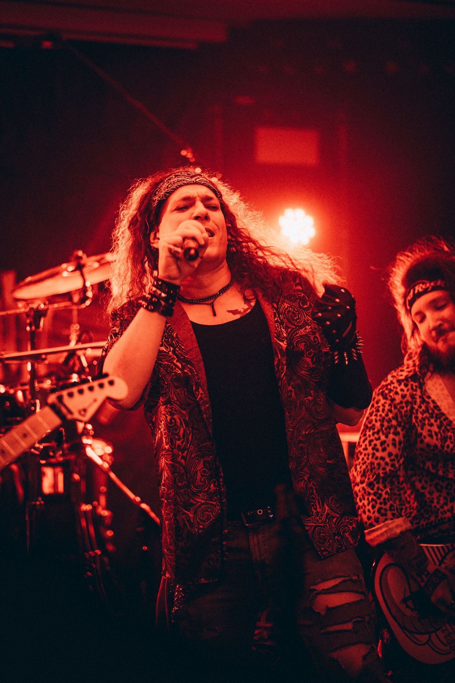 Long-haired rock vocalist singing passionately on stage under warm red concert lights.