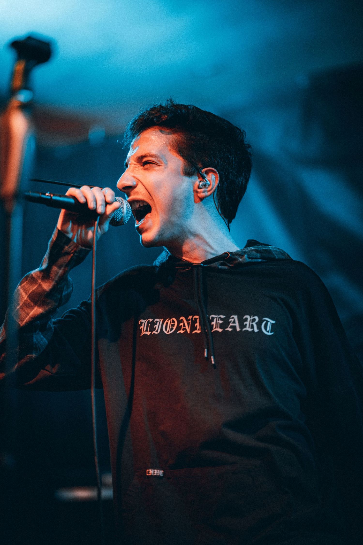 Male vocalist in black hoodie singing passionately into microphone at a live concert.