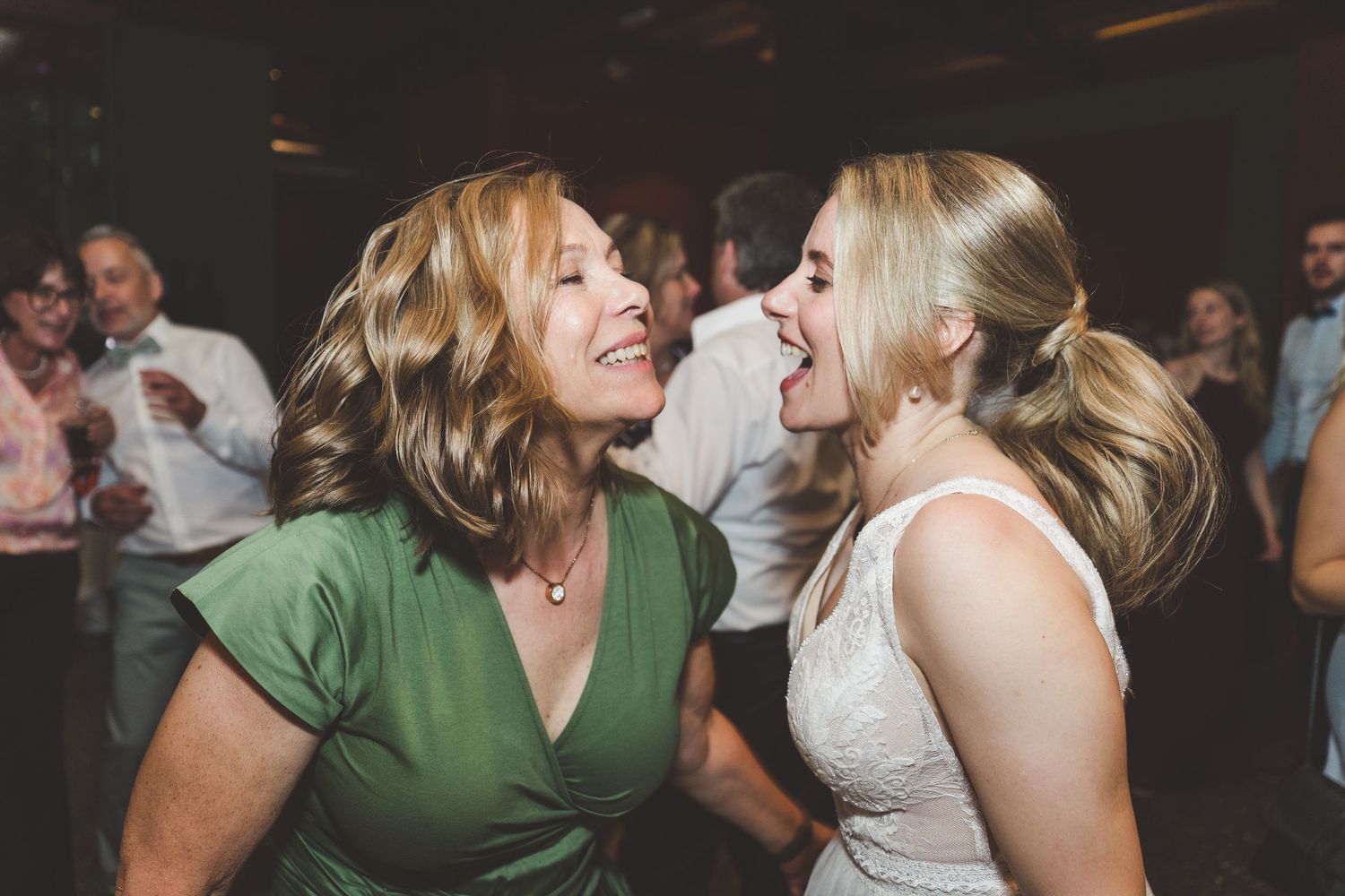 Two women laughing and dancing joyfully together at a wedding reception on the dance floor.