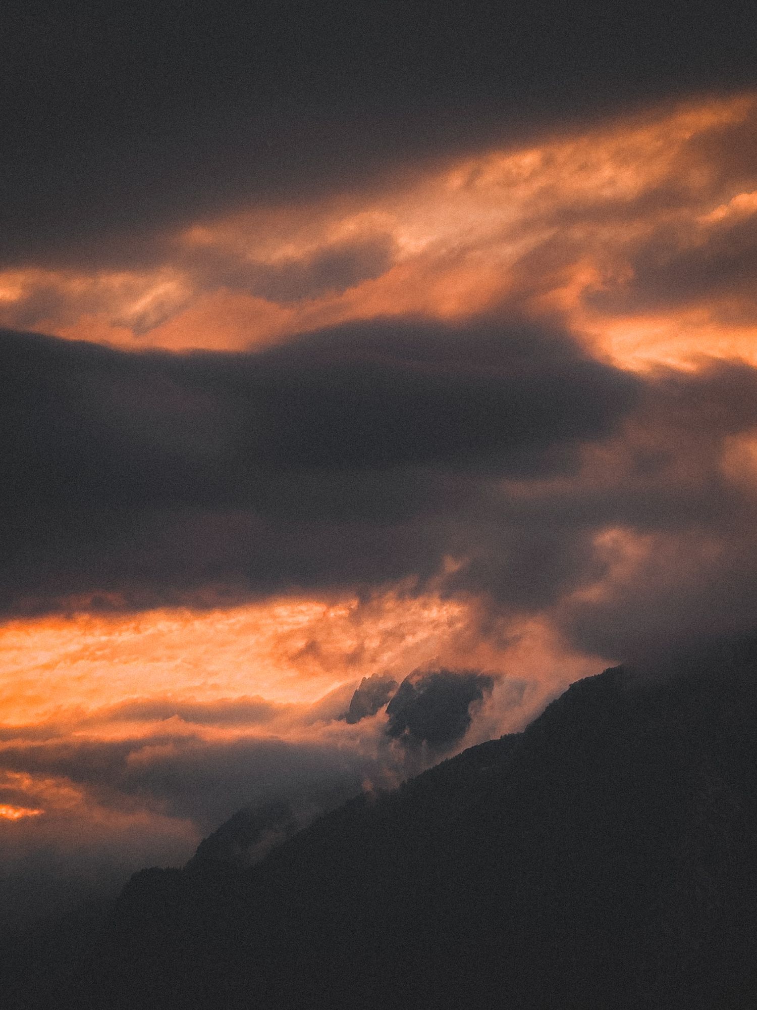 Dramatic orange and red sunset clouds illuminating mountain peaks with dark moody atmospheric sky.