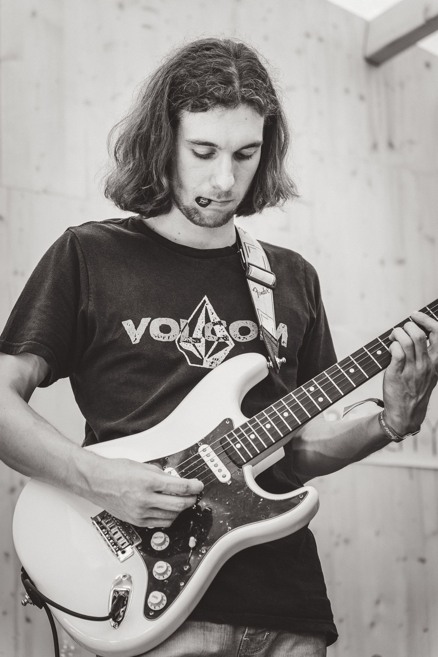 Black and white photo of long-haired guitarist playing white Stratocaster in Volcom t-shirt.