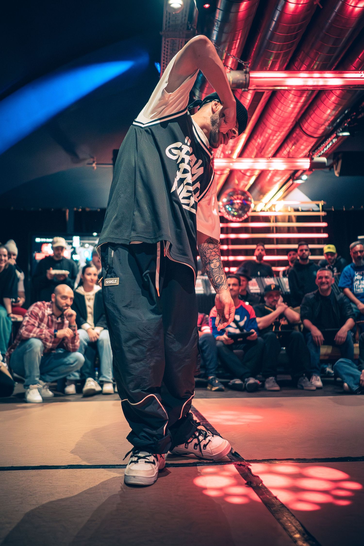 B-boy in oversized streetwear poses confidently on stage at a hip-hop dance battle event.