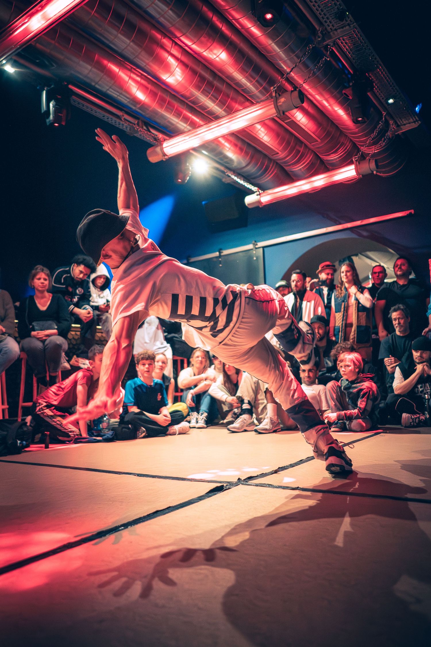 Breakdancer executes a gravity-defying freeze under red neon lights at a hip-hop battle event.