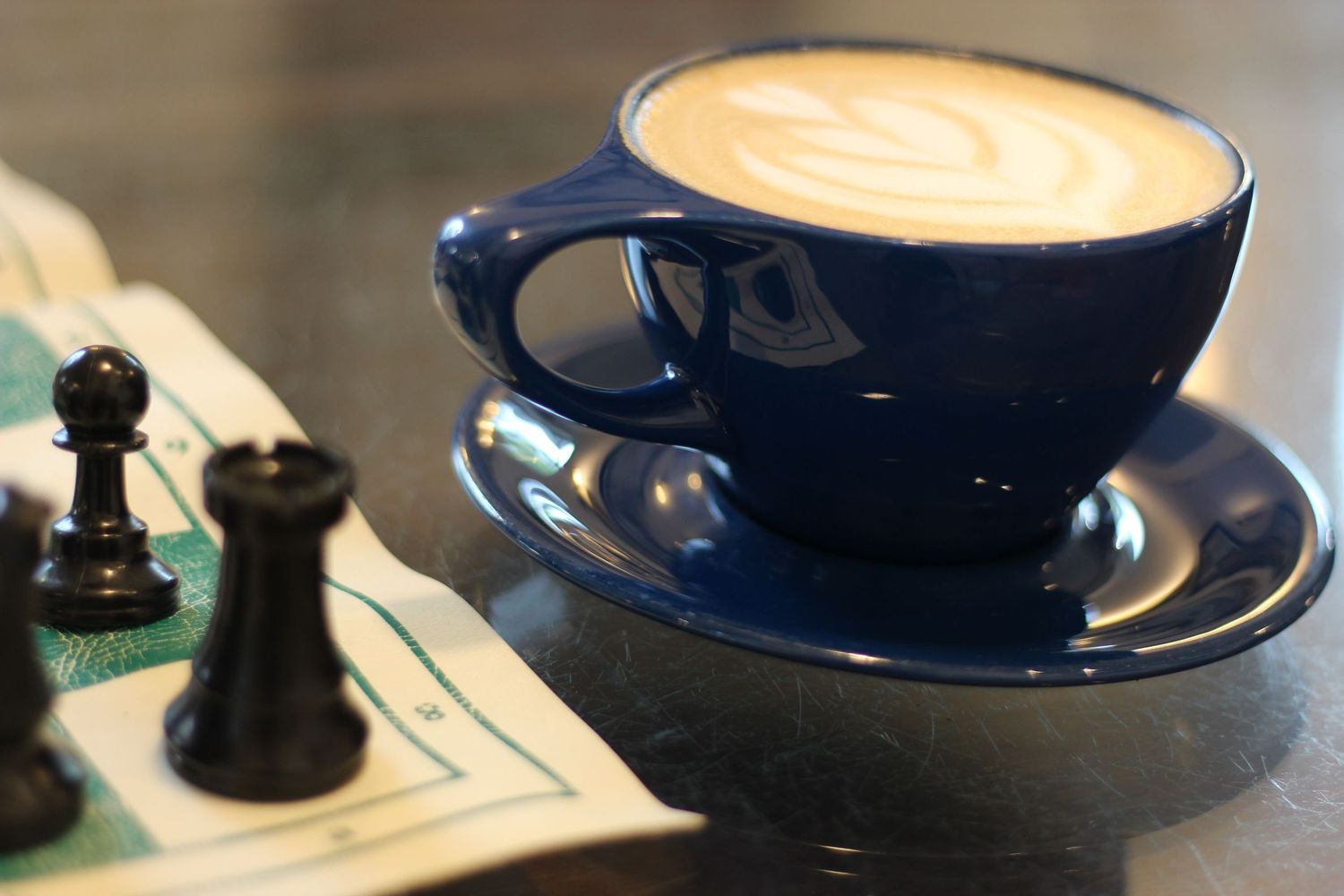 A photo of a cup of coffee with a chess set next to it