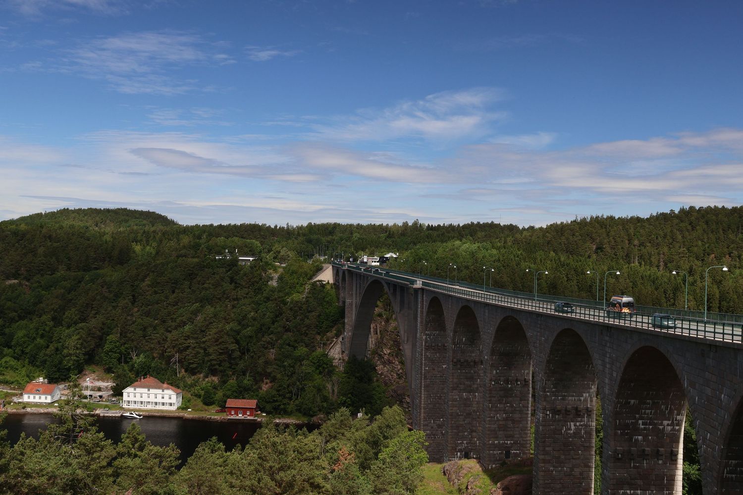 A historic stone viaduct bridge with arches spans a forested valley under a blue sky.