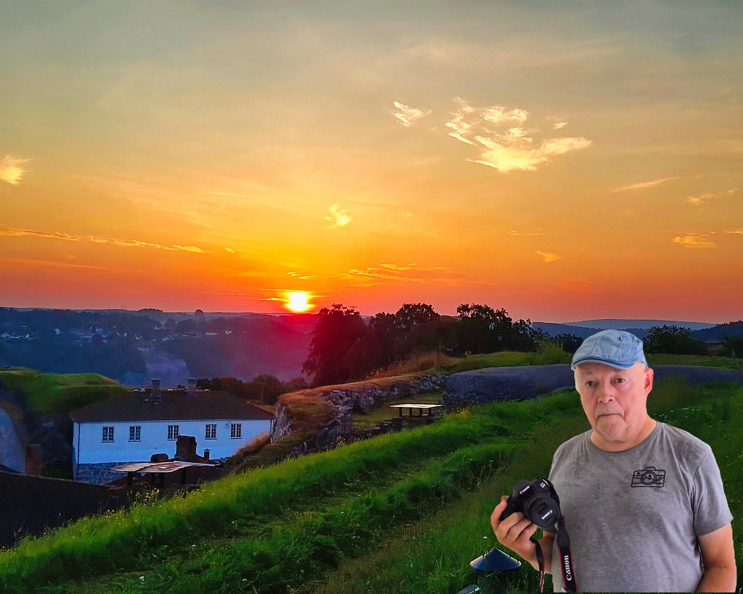 Photographer holding camera at golden sunset overlooking green hillside valley with dramatic orange sky.