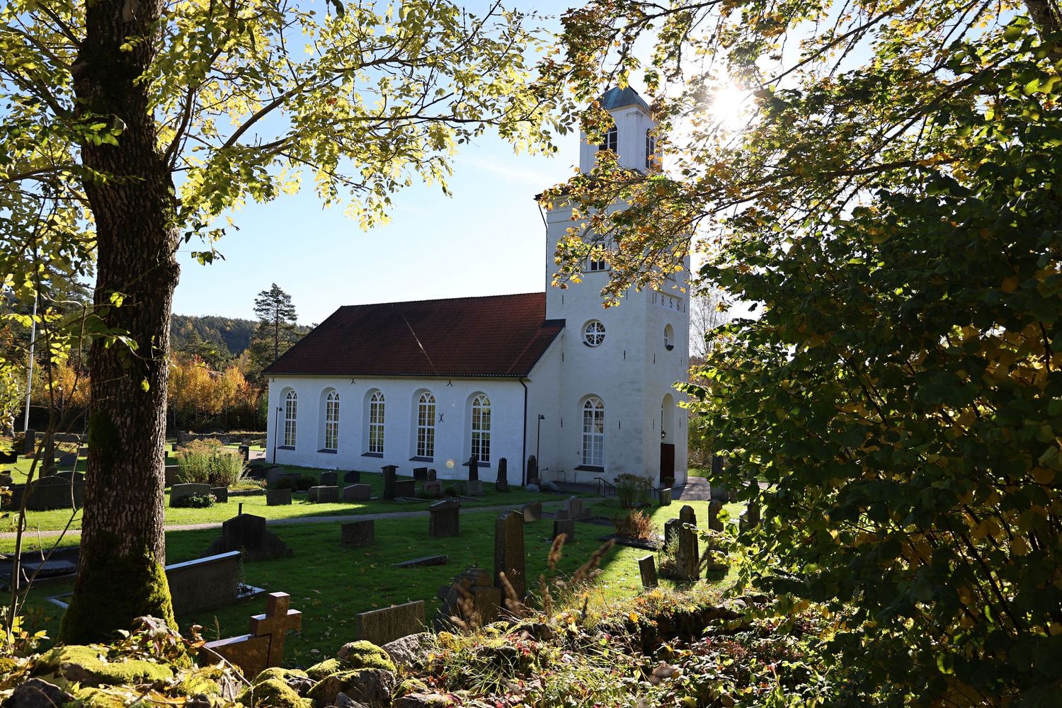 White church with bell tower surrounded by autumn trees and a historic cemetery on a sunny day.
