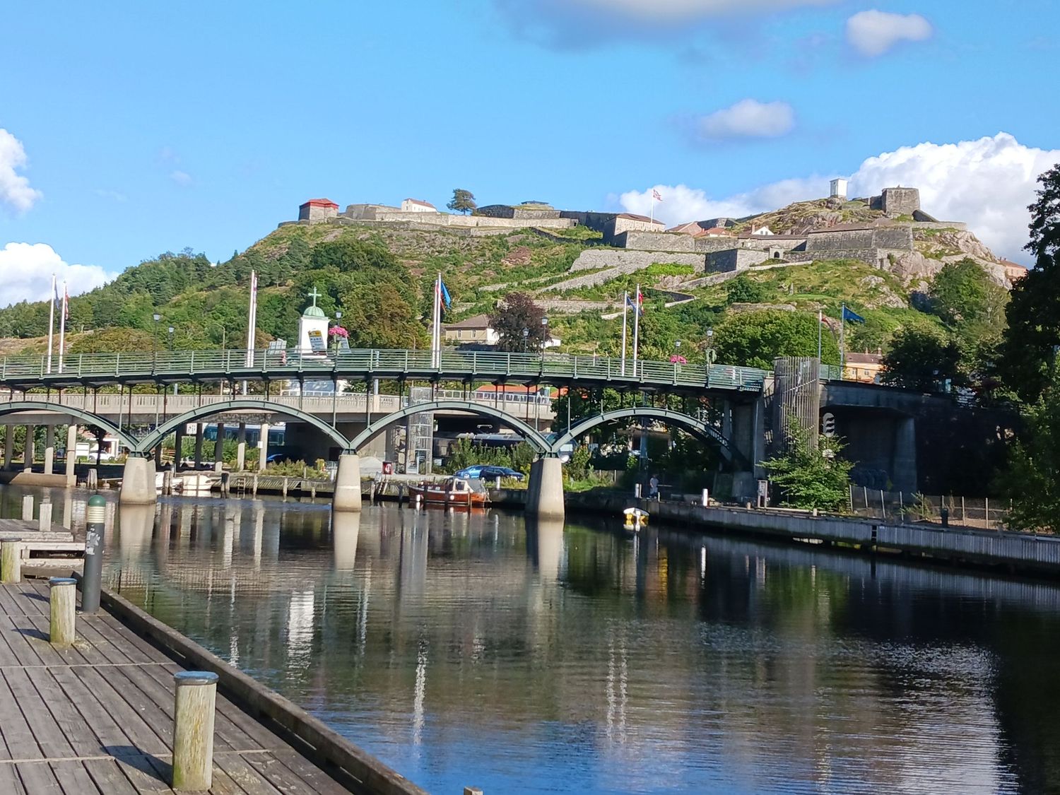 A scenic bridge over calm river waters with a historic hilltop fortress under blue skies.