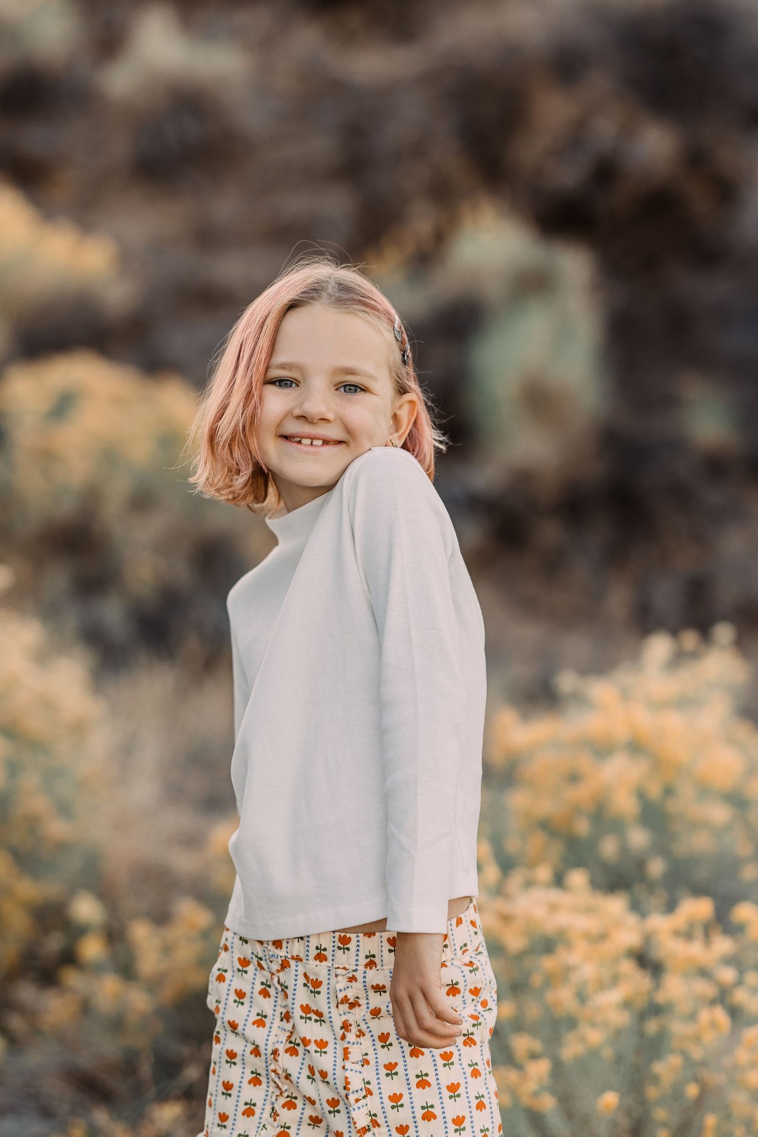 Happy young girl with pink hair in white top and floral skirt smiling in wildflower field.