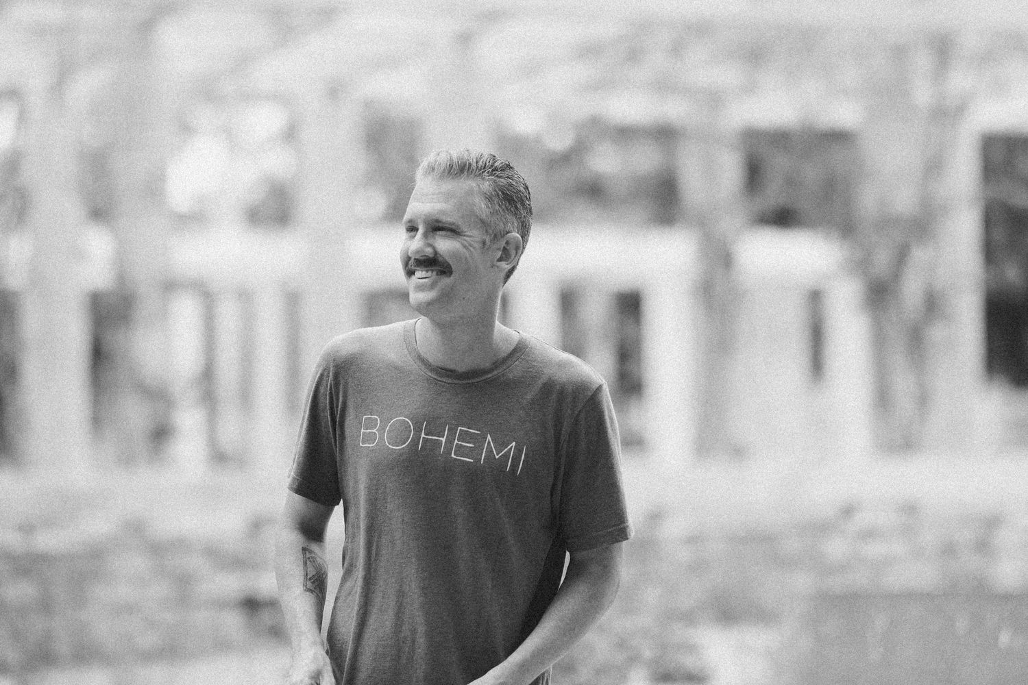 Smiling man wearing a Bohemi t-shirt photographed in black and white outdoors.