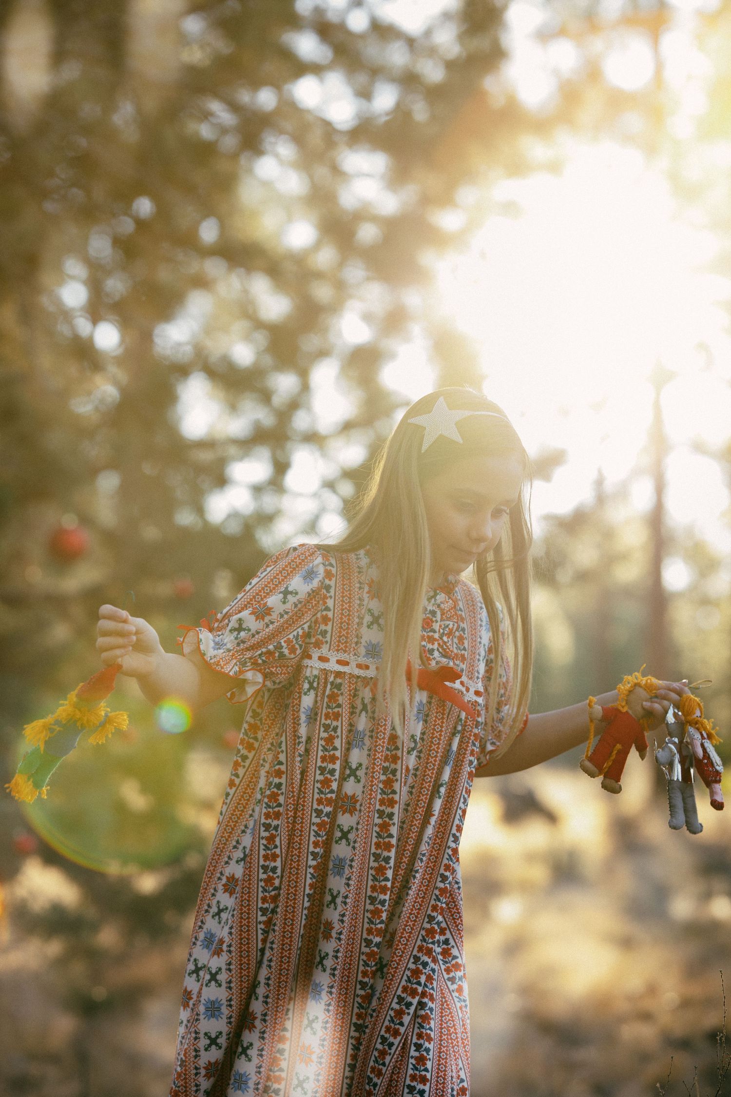 Young girl in boho patterned dress holding autumn leaves in sunlit forest.