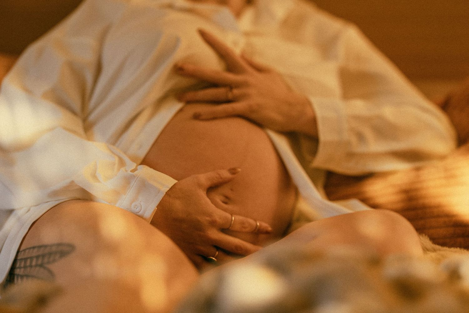 Close-up of pregnant woman in white sheer robe gently cradling her bare baby bump in warm golden light.