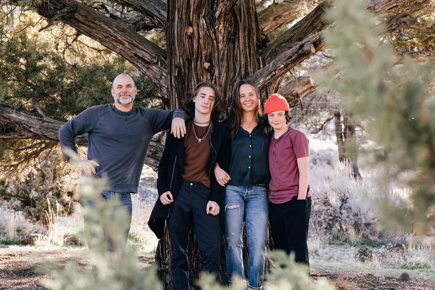Family of four posing together in front of a large tree outdoors.