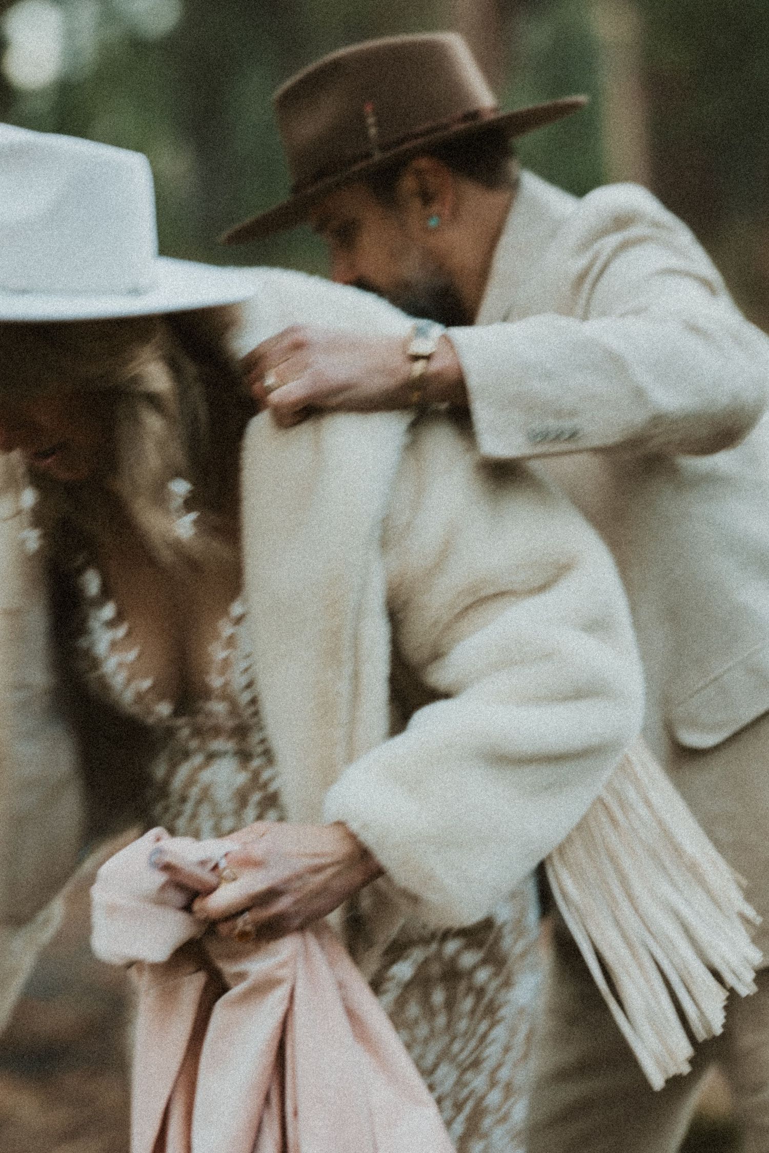 Couple in boho wedding attire share an intimate moment in a forest setting.