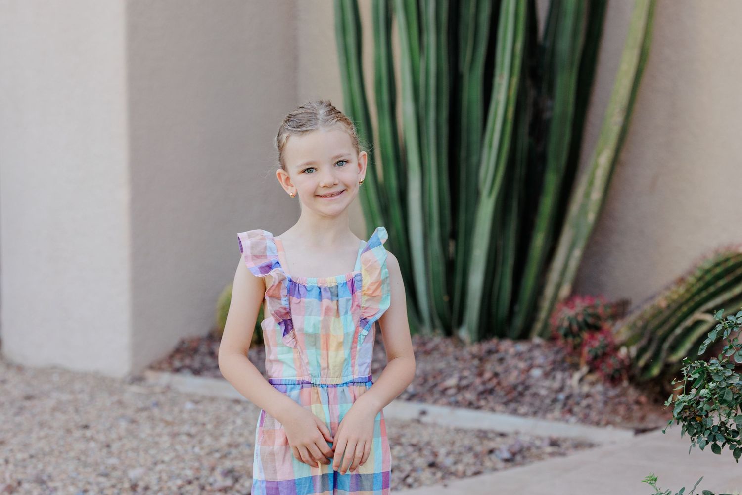 Smiling young girl in pastel plaid dress posing in front of cactus garden.