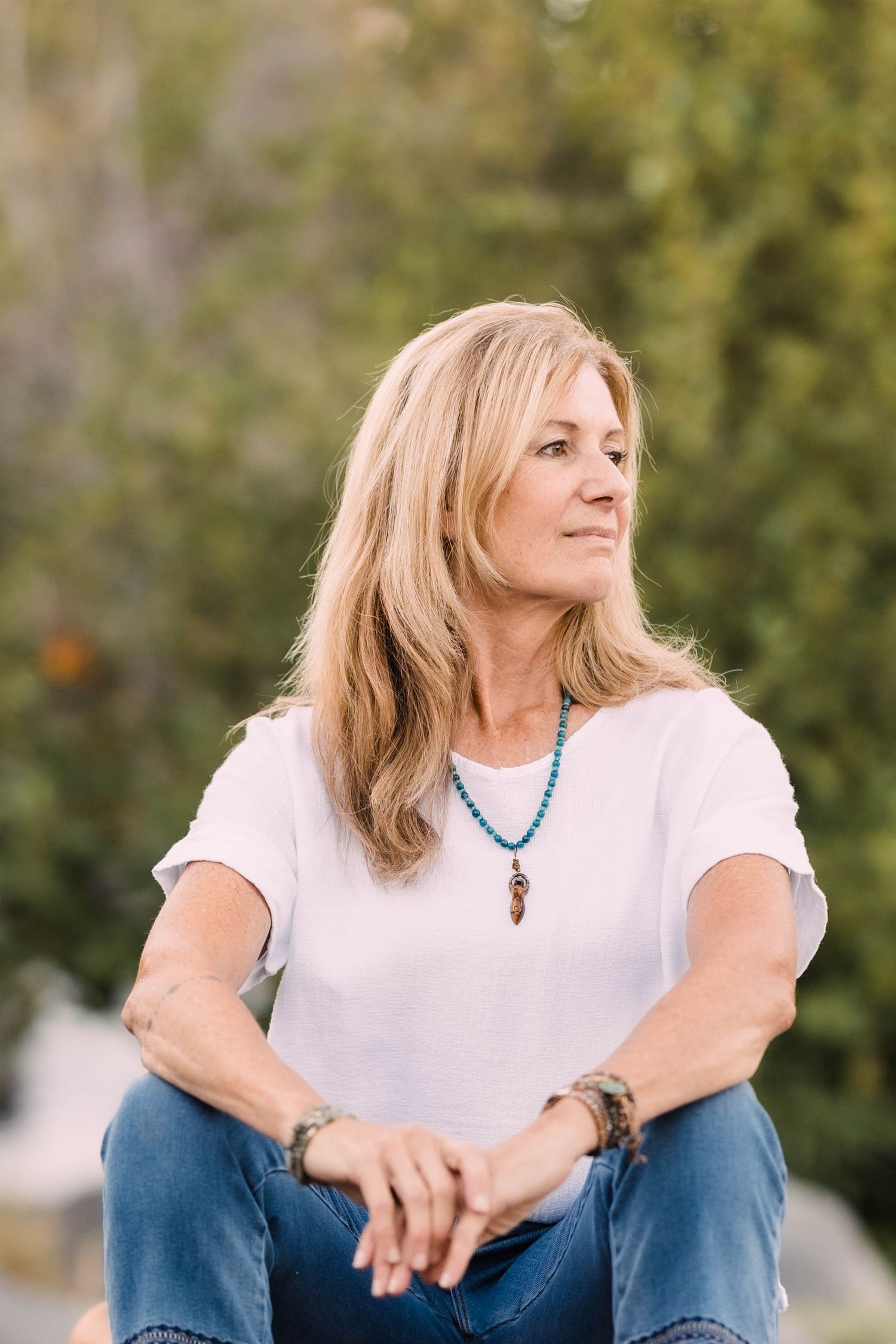 Blonde woman in white tee and jeans sitting outdoors.