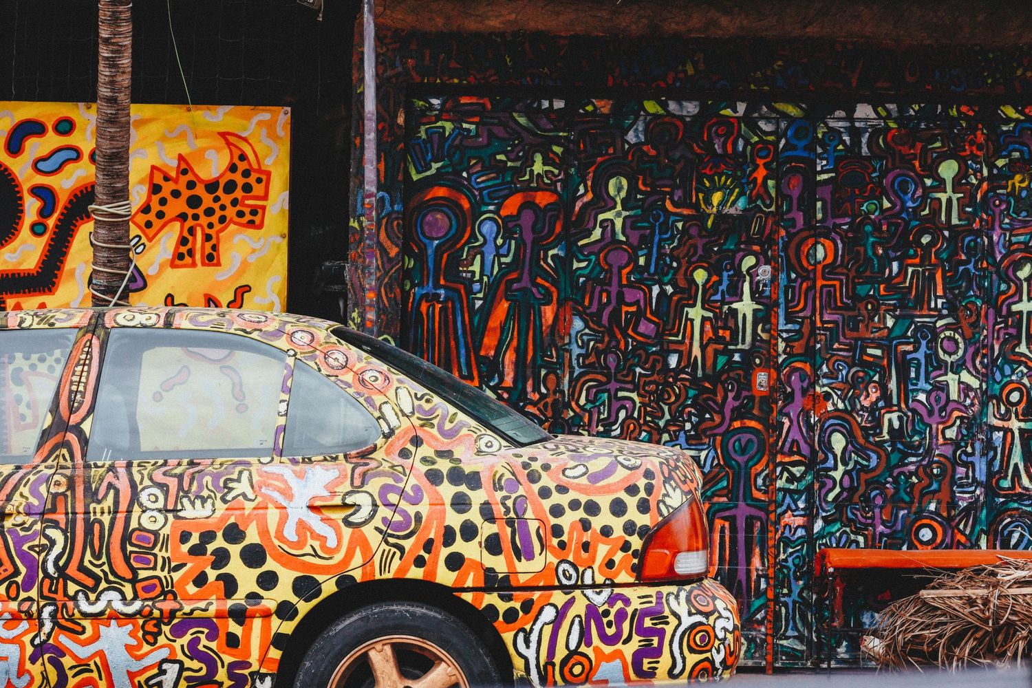 Vividly painted car covered in colorful graffiti art parked in front of a street mural.