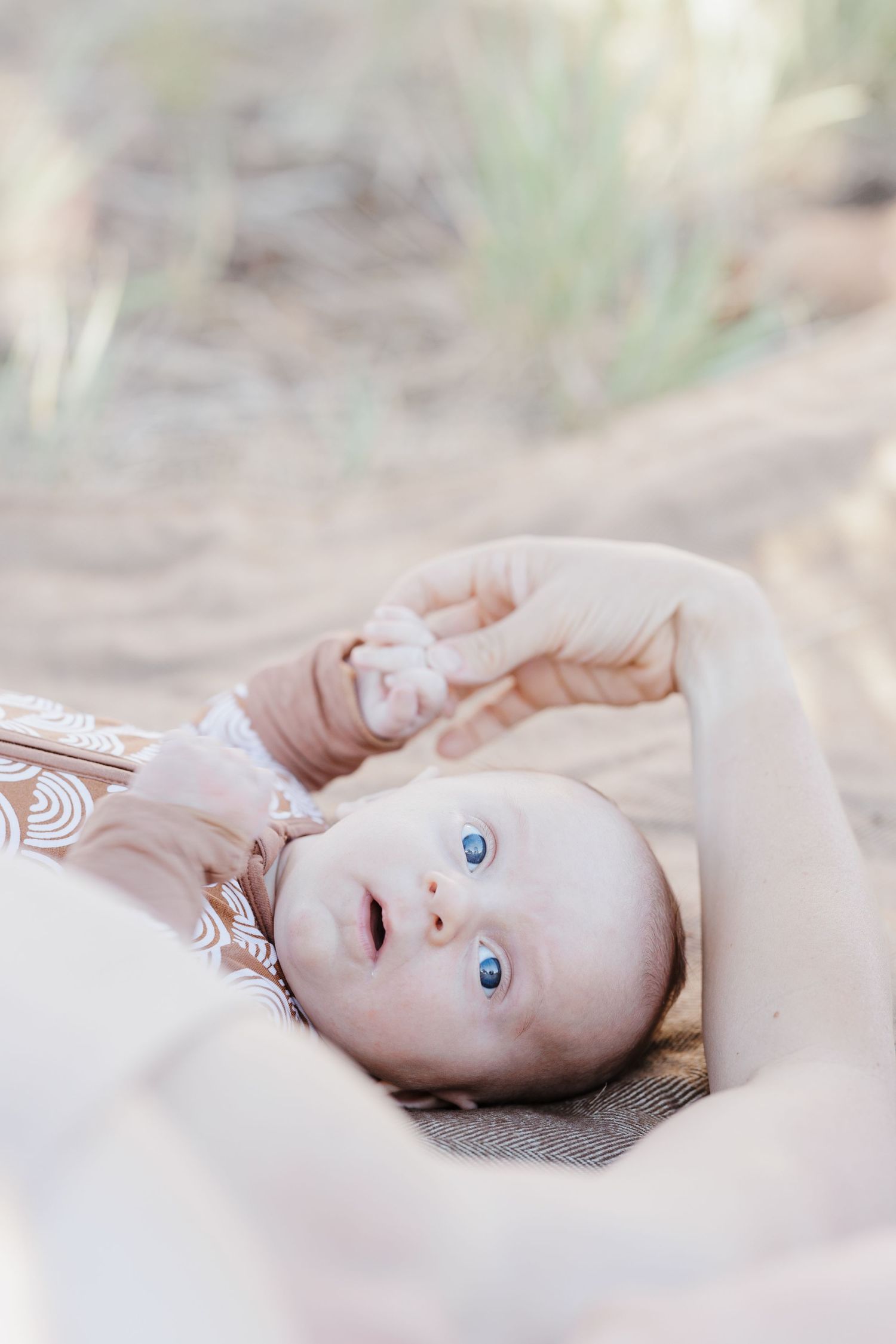 Blue-eyed baby in pink outfit lying on lap outdoors in natural desert setting.