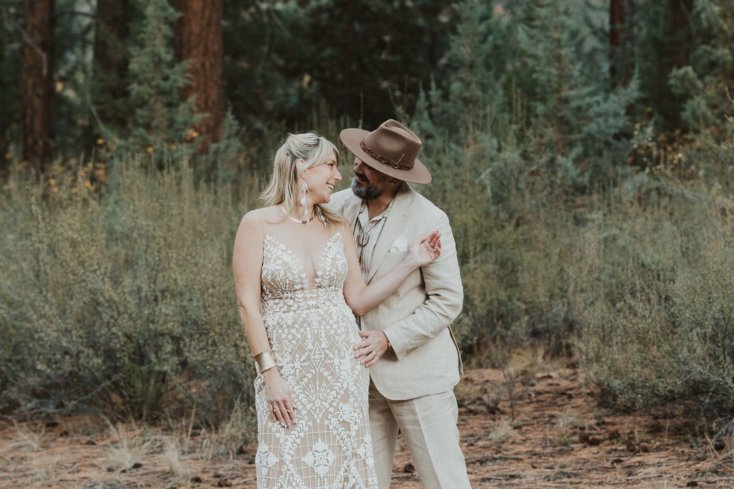 Bohemian couple in elegant attire sharing a romantic moment in a forest setting.