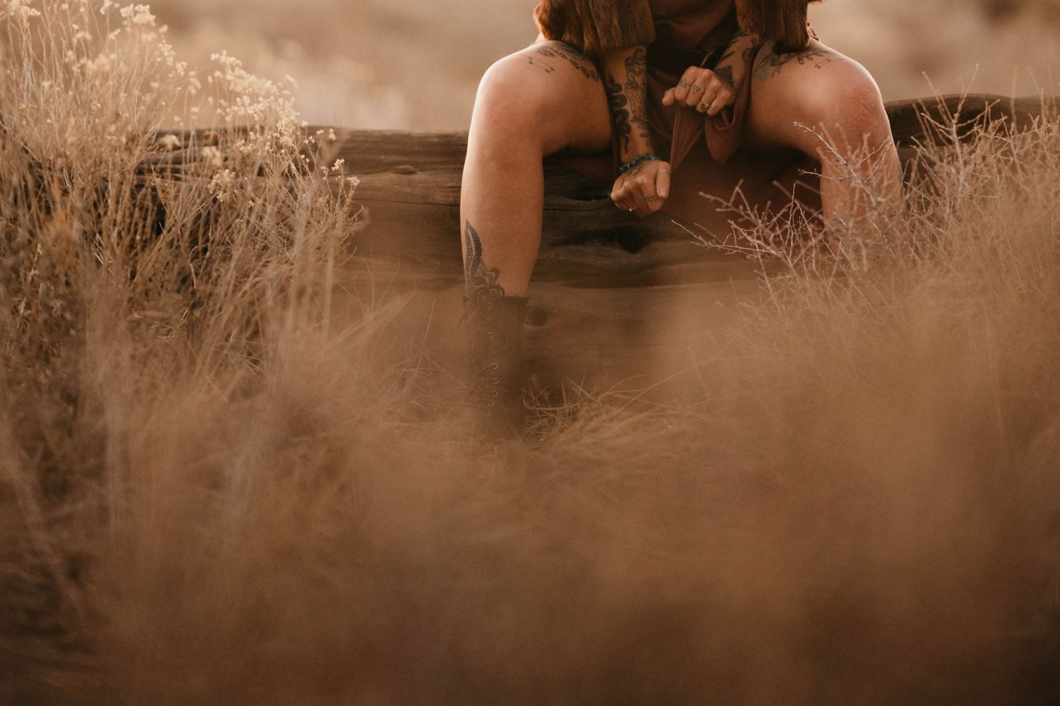 Close-up of person sitting on wooden beam surrounded by dry golden grass outdoors.