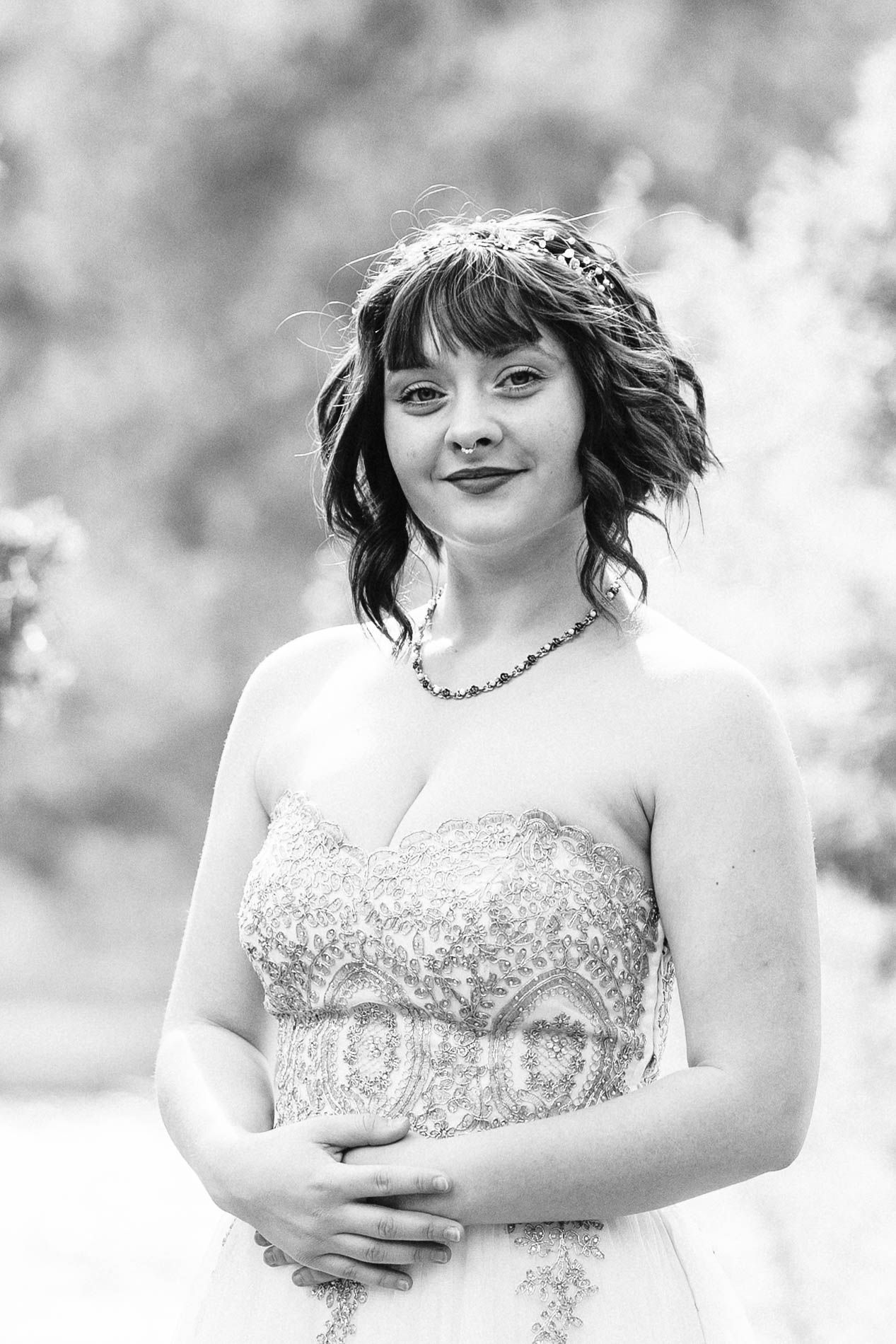 Black and white portrait of bride in strapless beaded gown with floral crown and necklace posing outdoors.