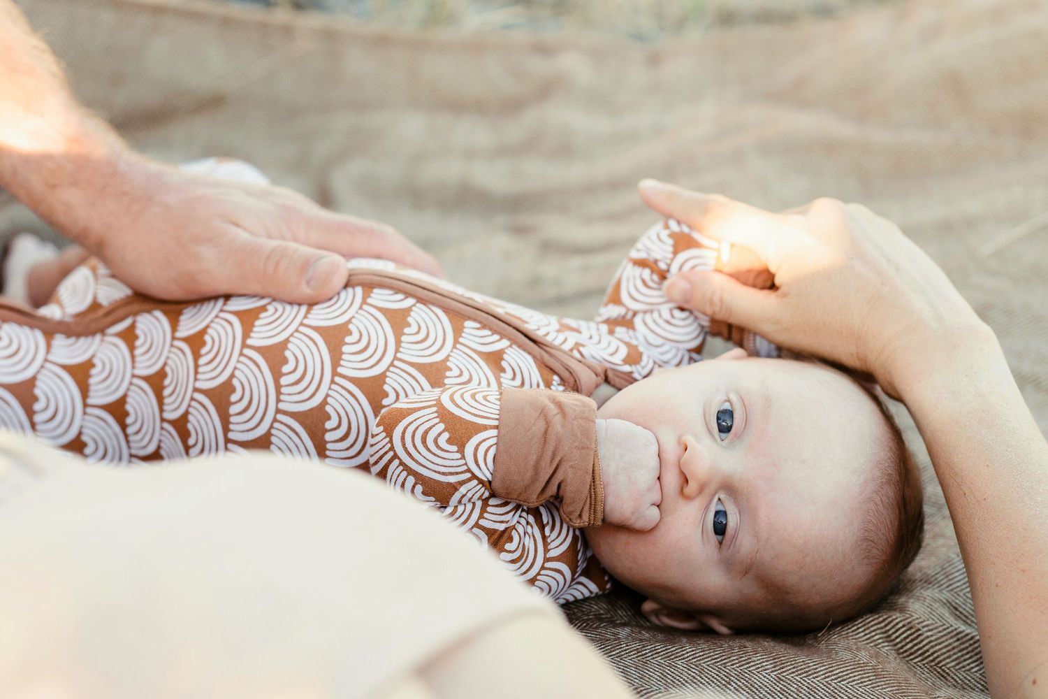Newborn baby in brown patterned onesie lying on a blanket held by parent.