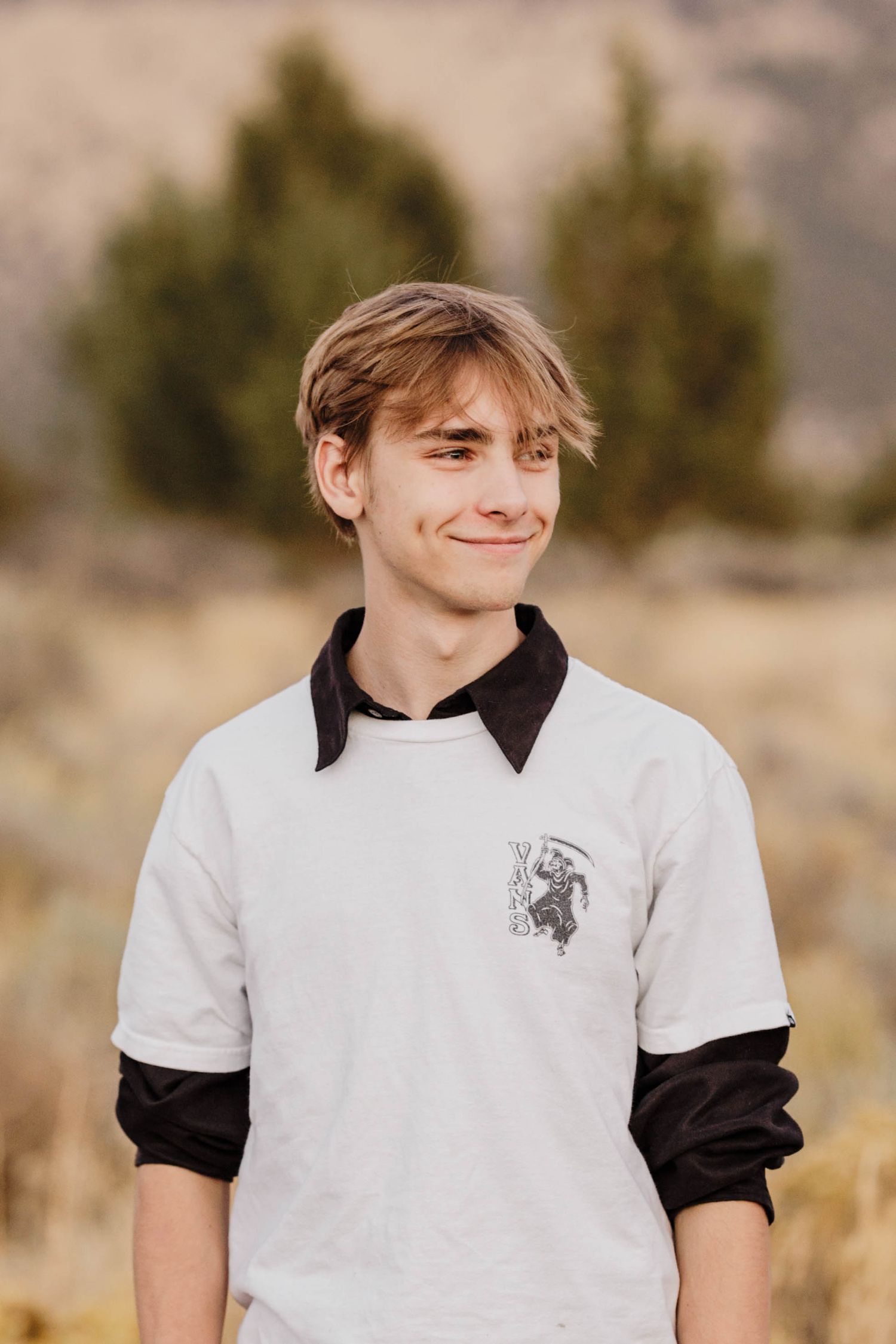Teenage boy with blonde hair smiling in white black layered shirt in nature.