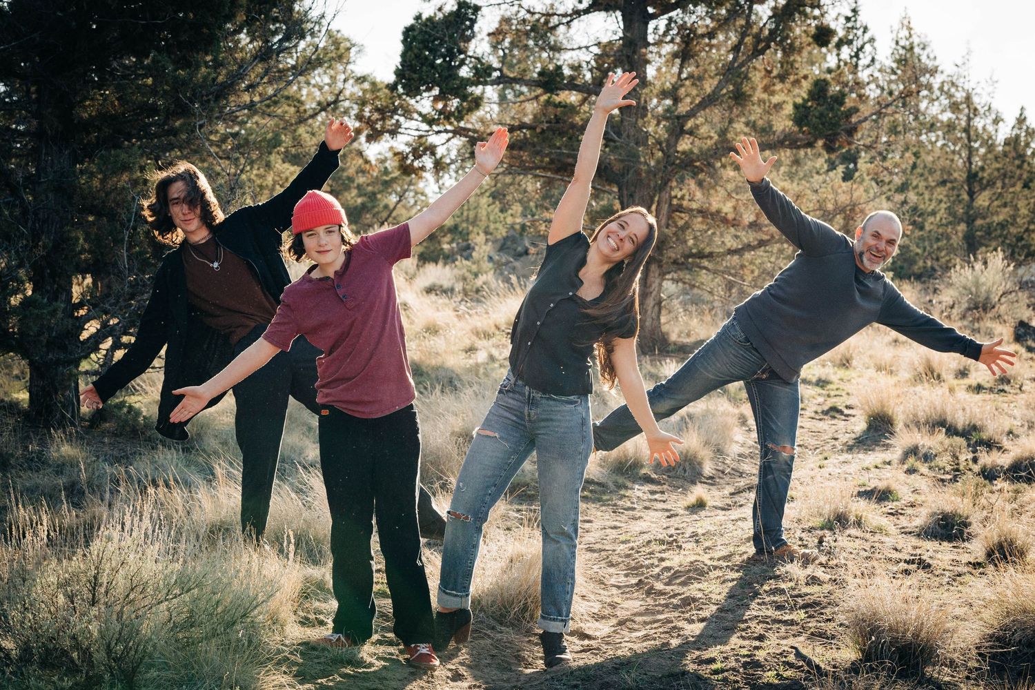 Playful family of four striking fun poses with arms outstretched outdoors.