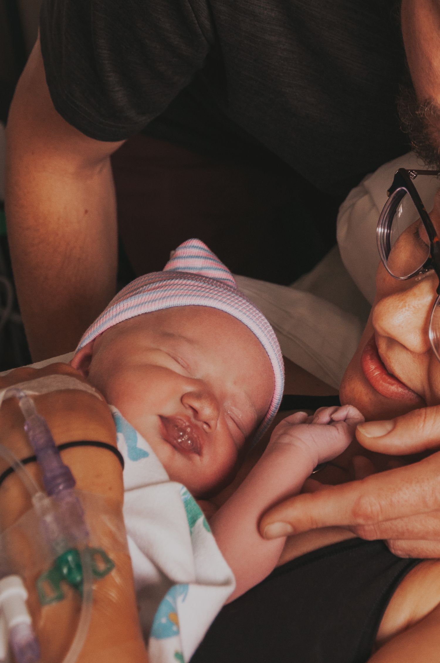 Newborn baby with medical tubes being held and kissed by parent wearing glasses in hospital.