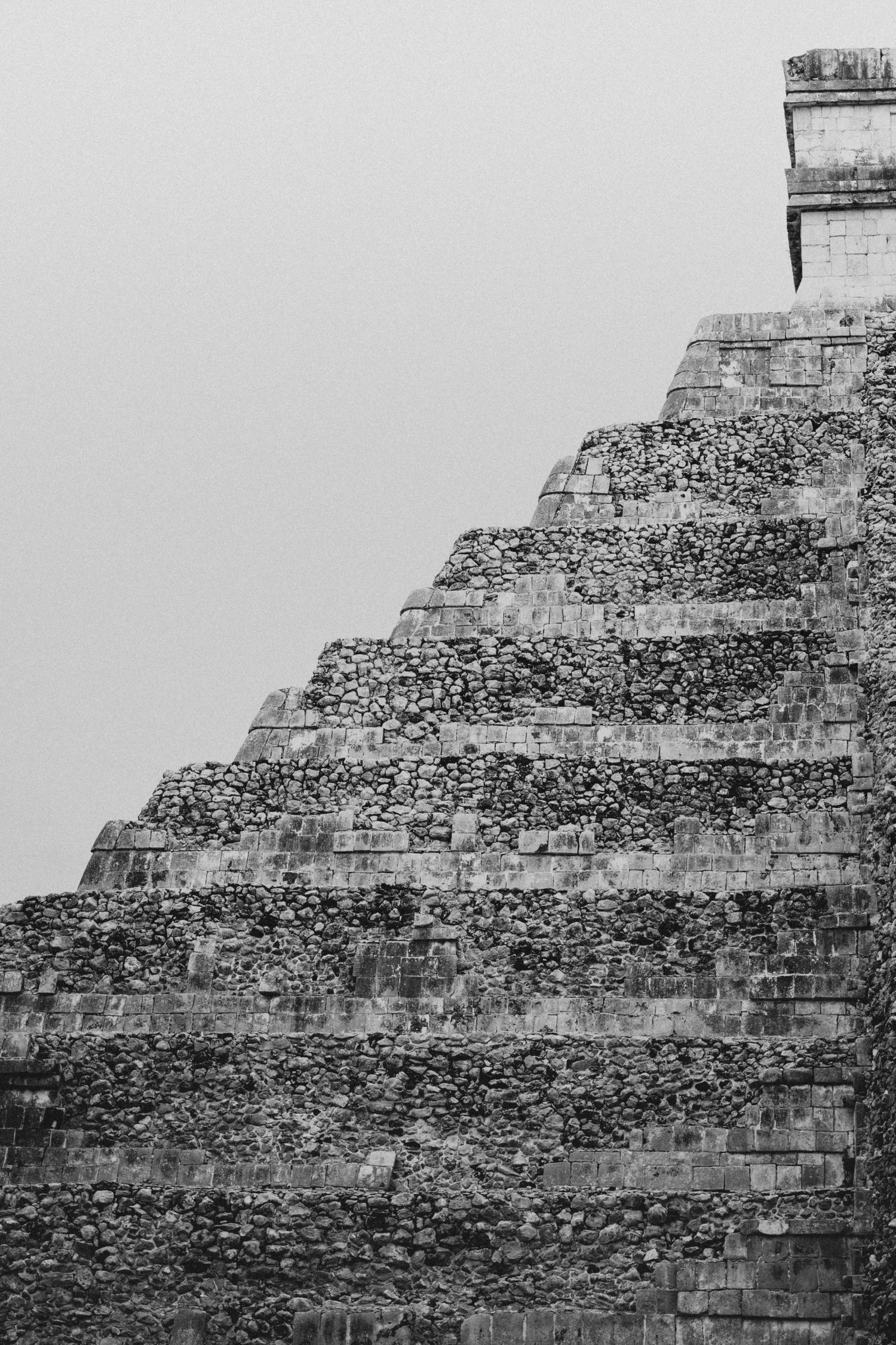 Black and white photo of ancient Mayan pyramid steps at Chichen Itza against grey sky.