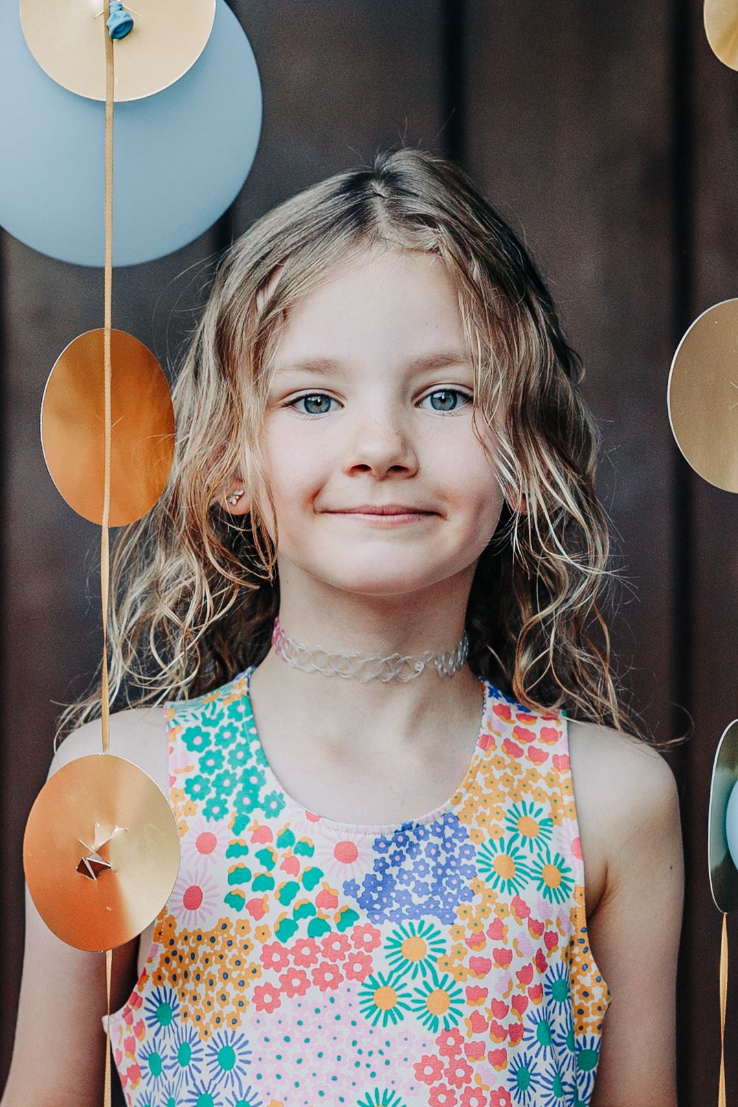 Young girl with blue eyes smiling in floral dress with colorful circle decorations.